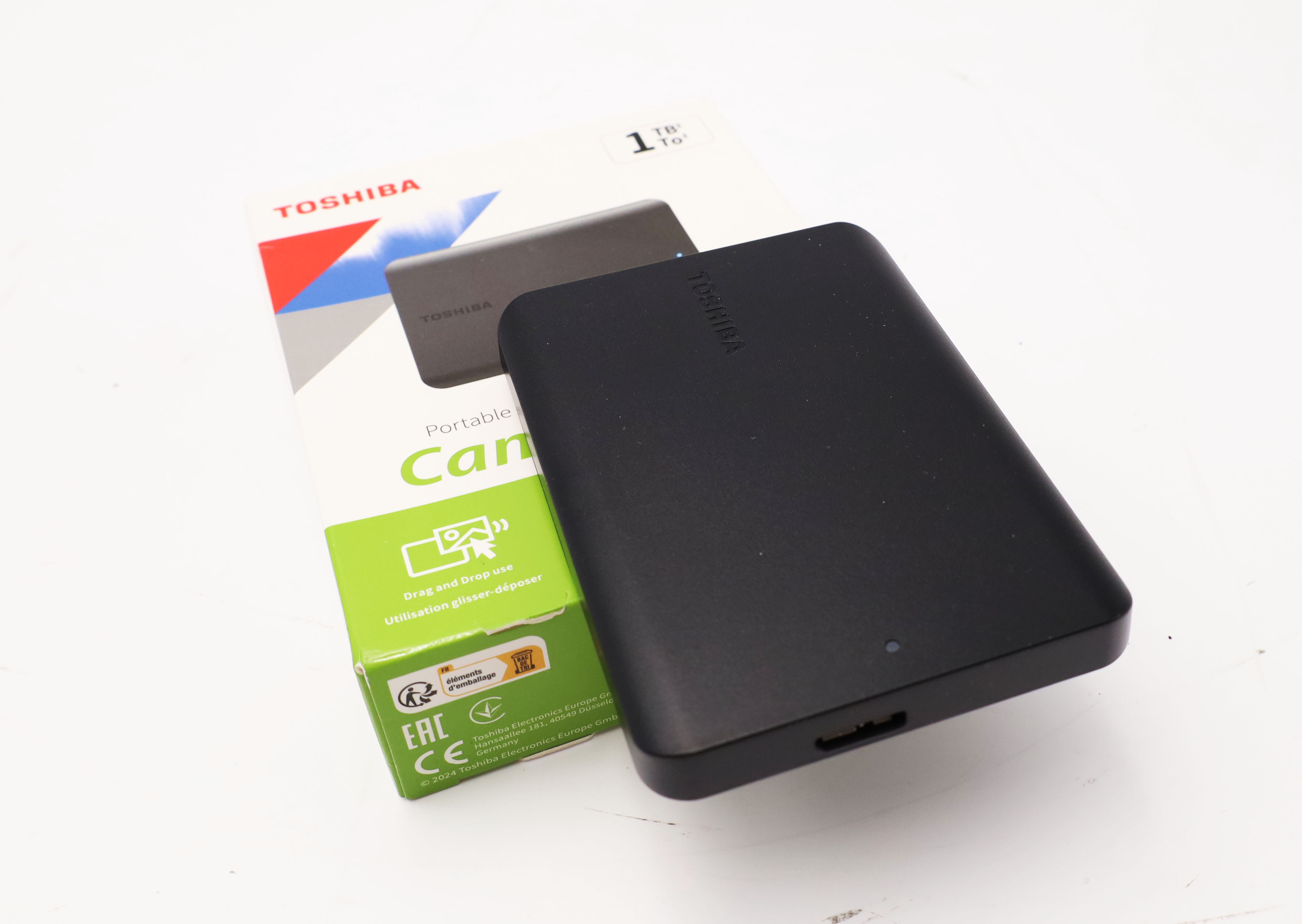 Hard disk esterno Toshiba nero accanto alla sua confezione con informazioni sul prodotto.