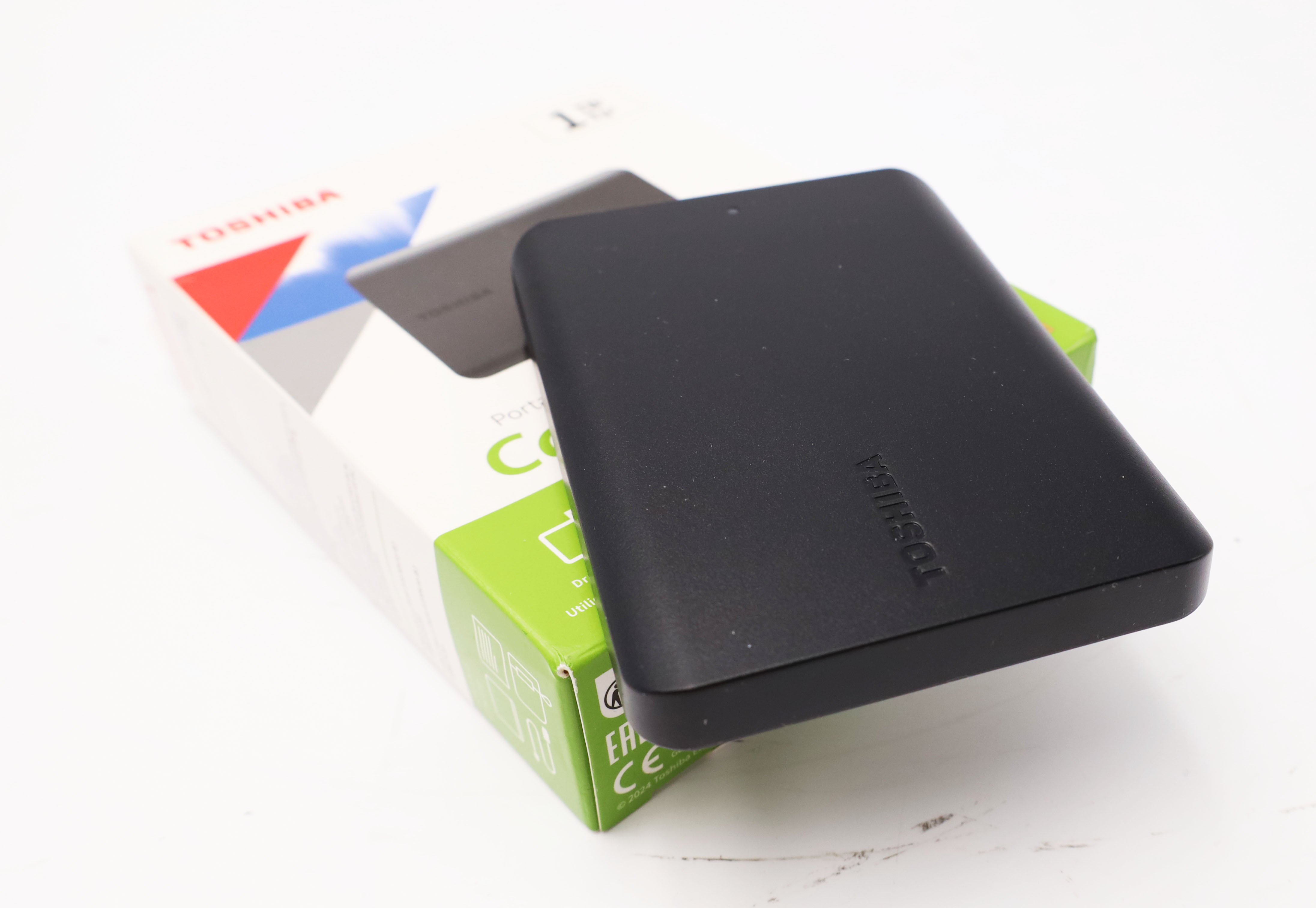 Hard disk esterno Toshiba nero accanto alla sua confezione con accenti verdi.