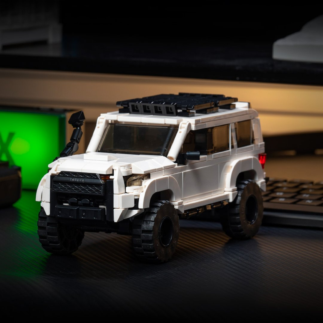 Biały SUV Lego z czarnymi akcentami i bagażnikiem dachowym stoi na biurku obok klawiatury.