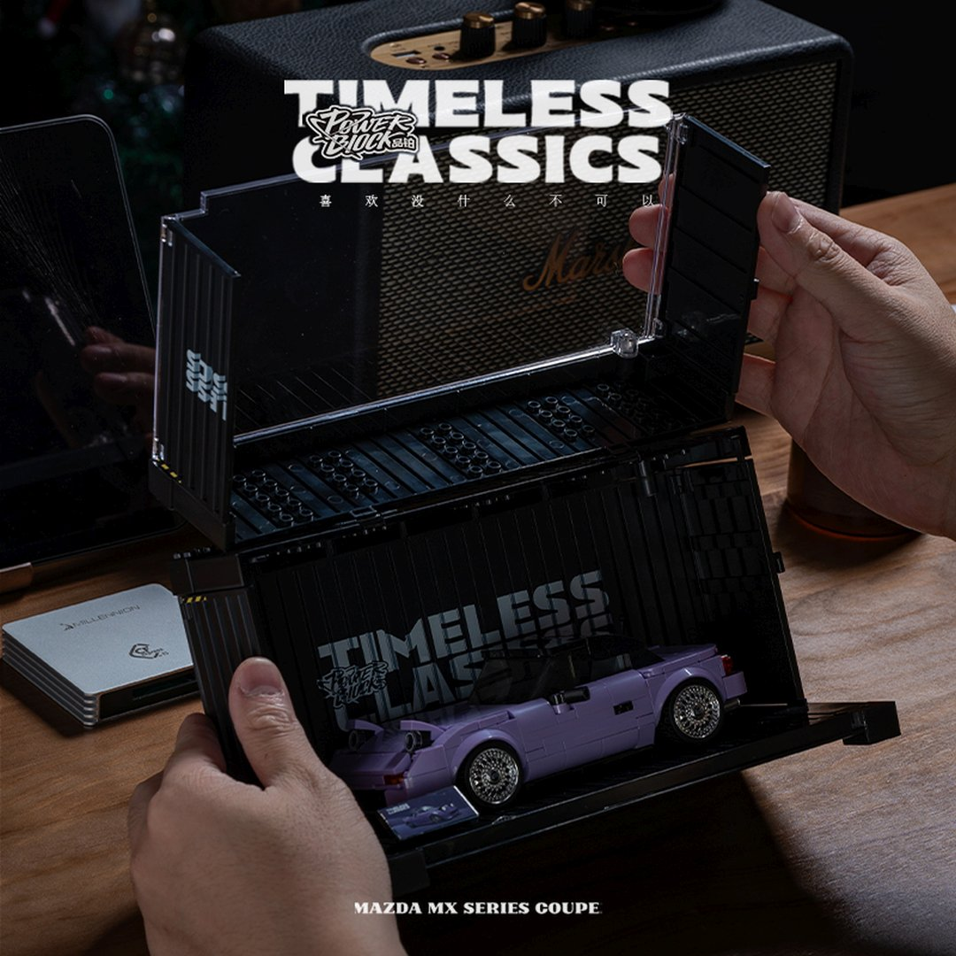 Dłonie otwierają czarne etui, ukazując fioletowy model Mazda MX coupe i napis 'Timeless Classics'.