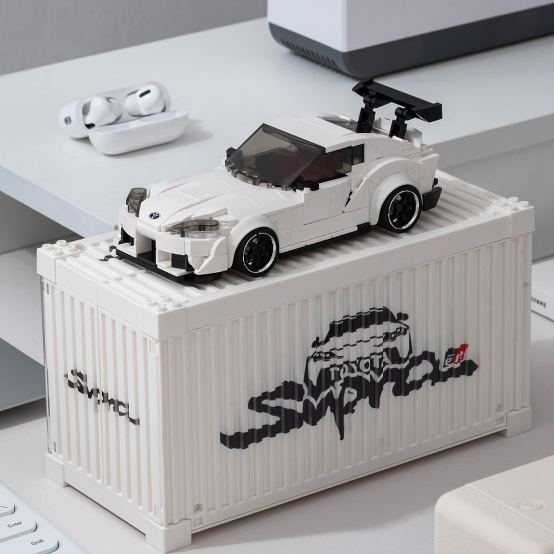 Biały Lego Supra na białym kontenerze z logo Supra. W pobliżu AirPods.
