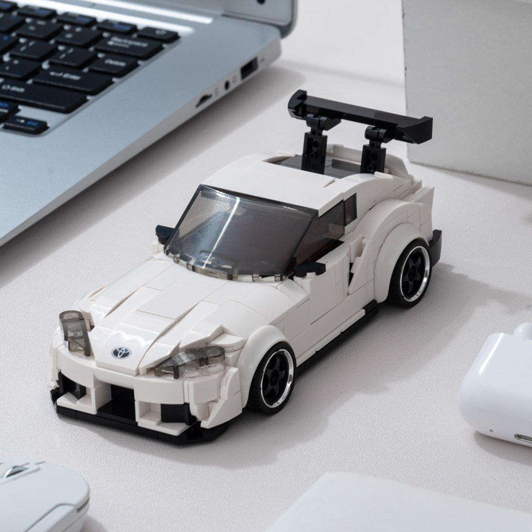 Biały samochód sportowy Lego ze spojlerem, obok laptopa, myszy i słuchawek.