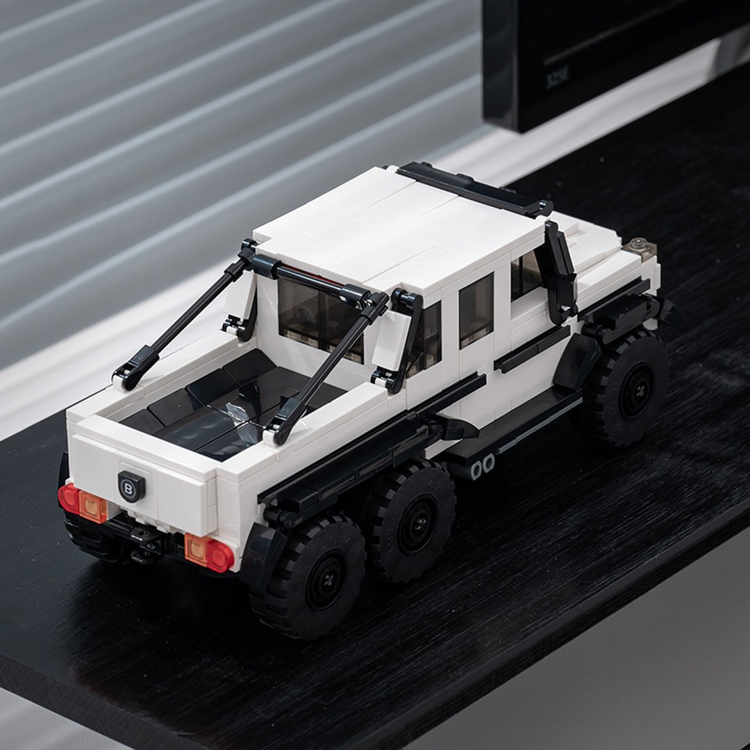 Biała ciężarówka Lego z sześcioma kołami i czarnymi akcentami, na czarnej powierzchni.