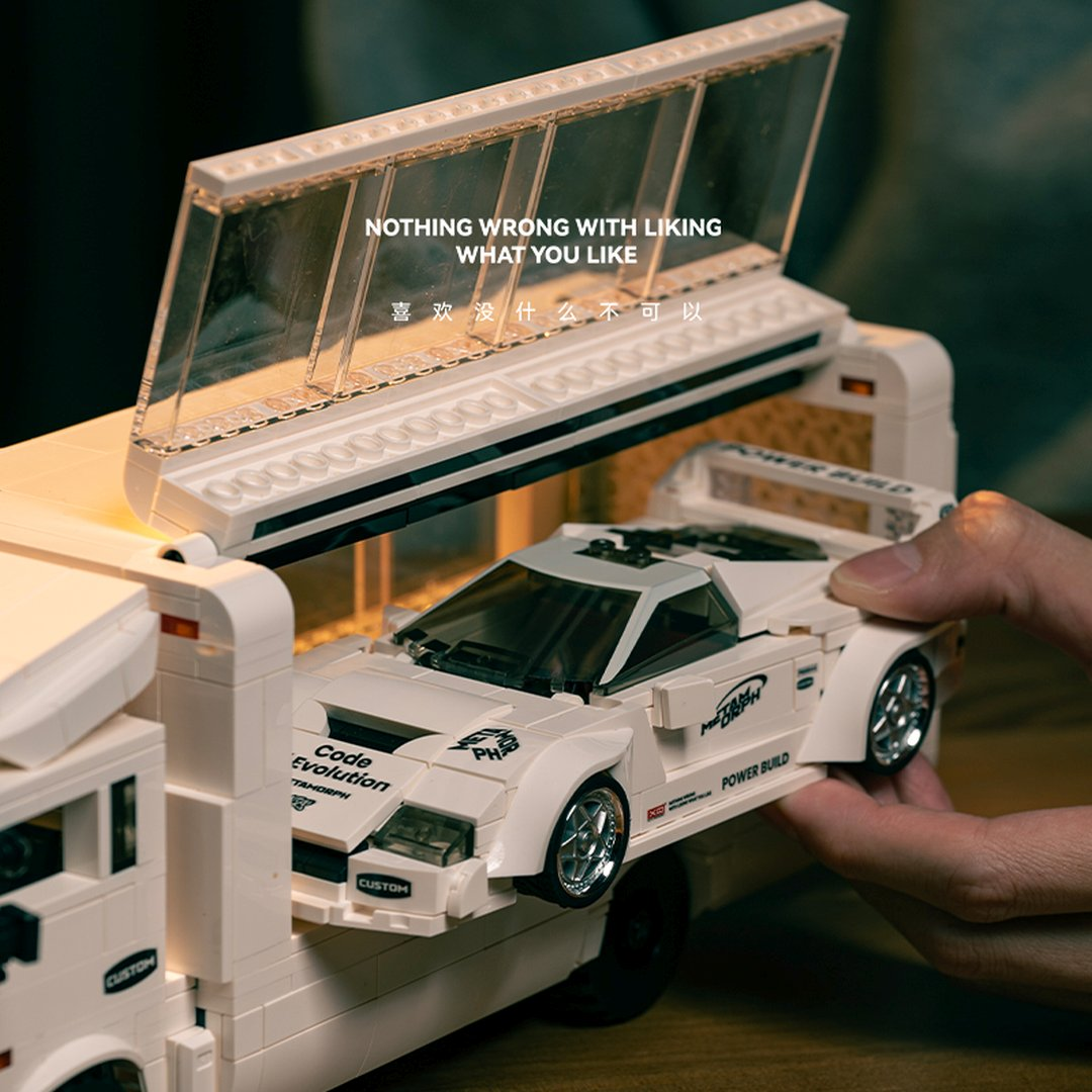 Biały samochód Lego jest ładowany do transportera. Na górze widoczny jest tekst.