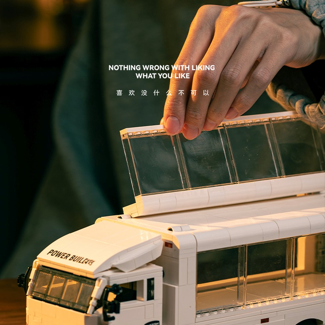 Ręka składa dach białego autobusu z klocków Lego. Napis: 'Nic złego w lubieniu tego, co lubisz.'