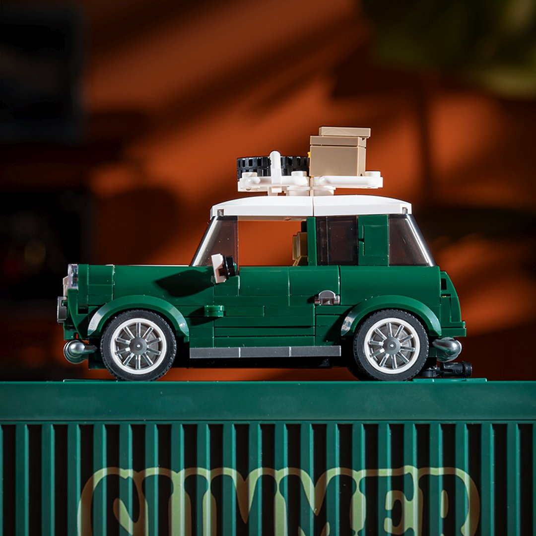 Zielony Mini Lego z białym dachem i bagażem na dachu stoi na zielonej skrzynce.