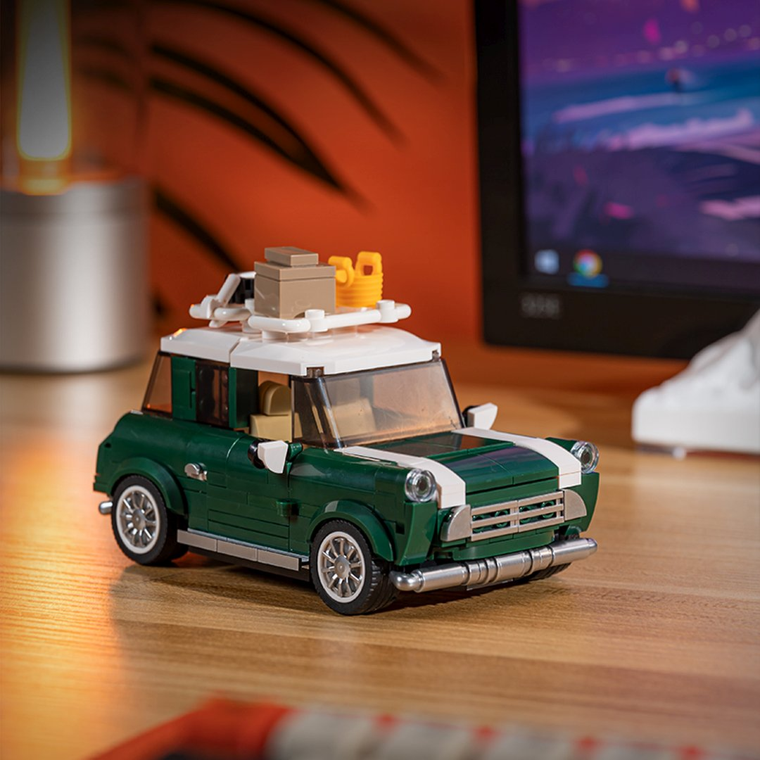 Zielone Lego Mini z białym dachem, bagażnikiem dachowym i bagażem na drewnianym stole.