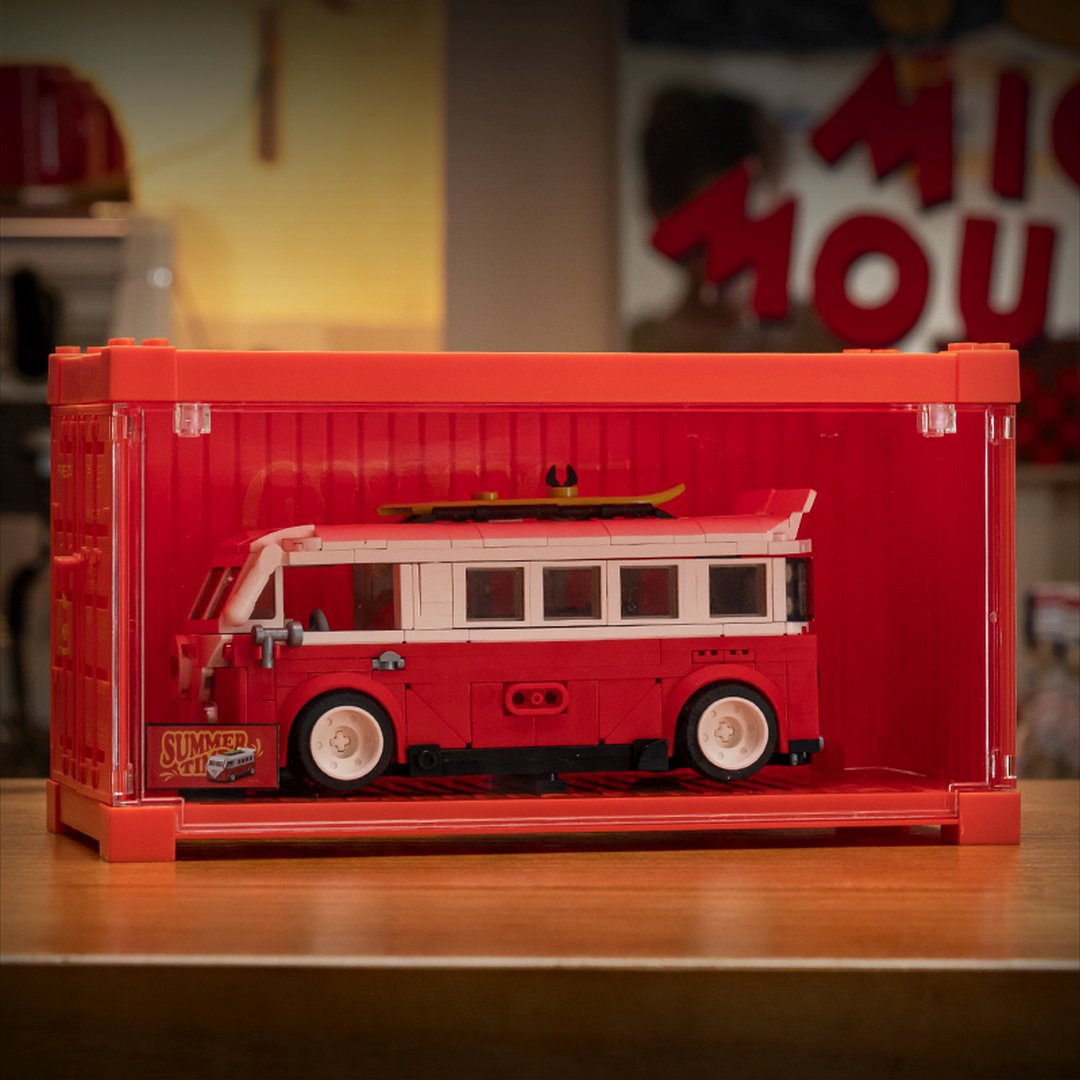 Czerwono-biały autobus Lego z deską surfingową na dachu, w czerwonym pudełku.