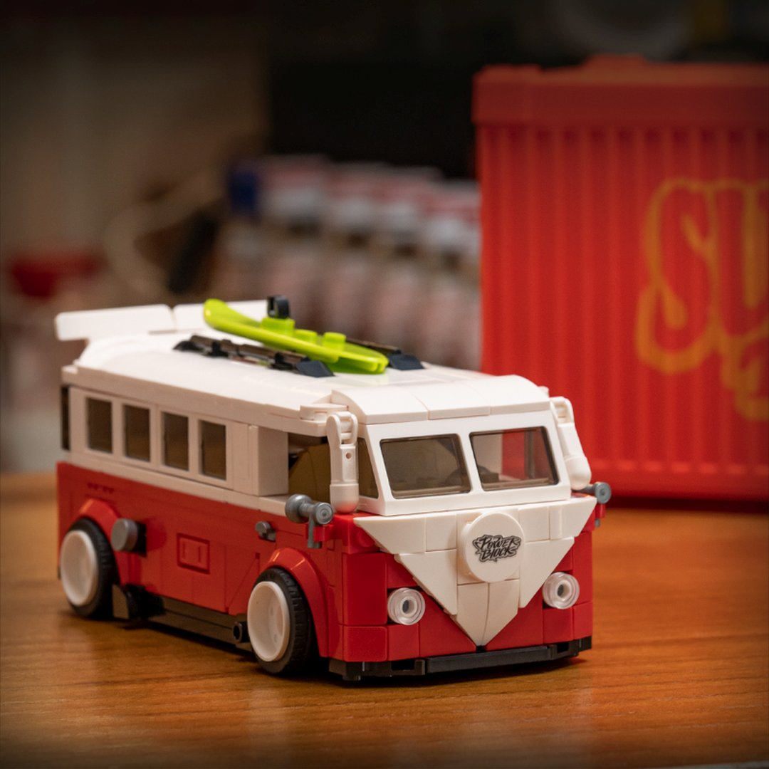 Czerwony i biały autobus Lego VW z deską surfingową na dachu stoi na drewnianym stole.
