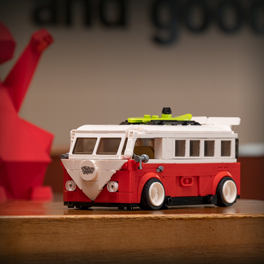 Czerwono-biała furgonetka Lego z deską surfingową na dachu, na drewnianym stole.