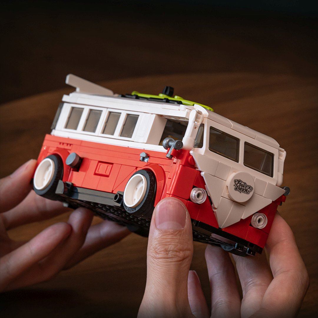 Ręka trzyma czerwono-białego busa Lego z białymi felgami.