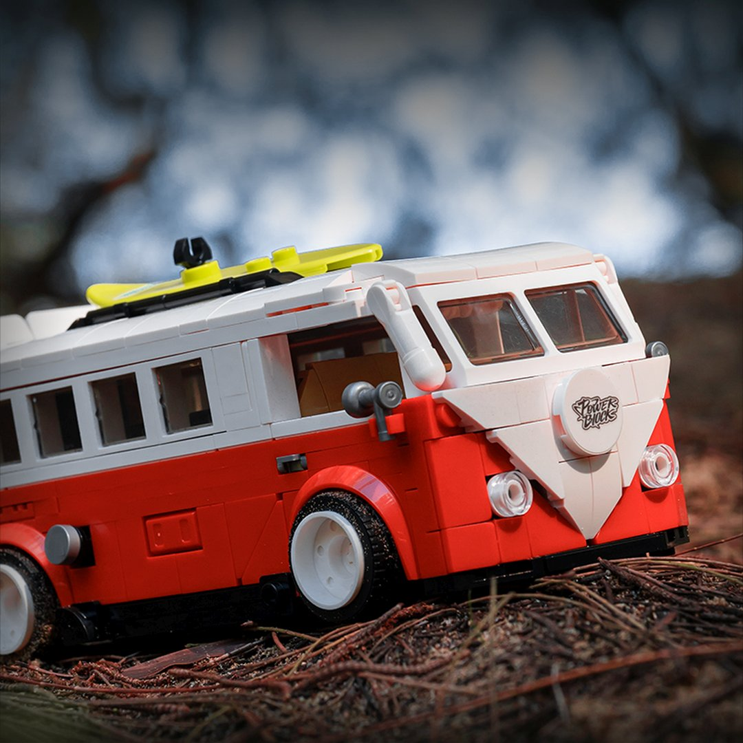 Czerwony i biały autobus Lego z deską surfingową na dachu stoi na zewnątrz.
