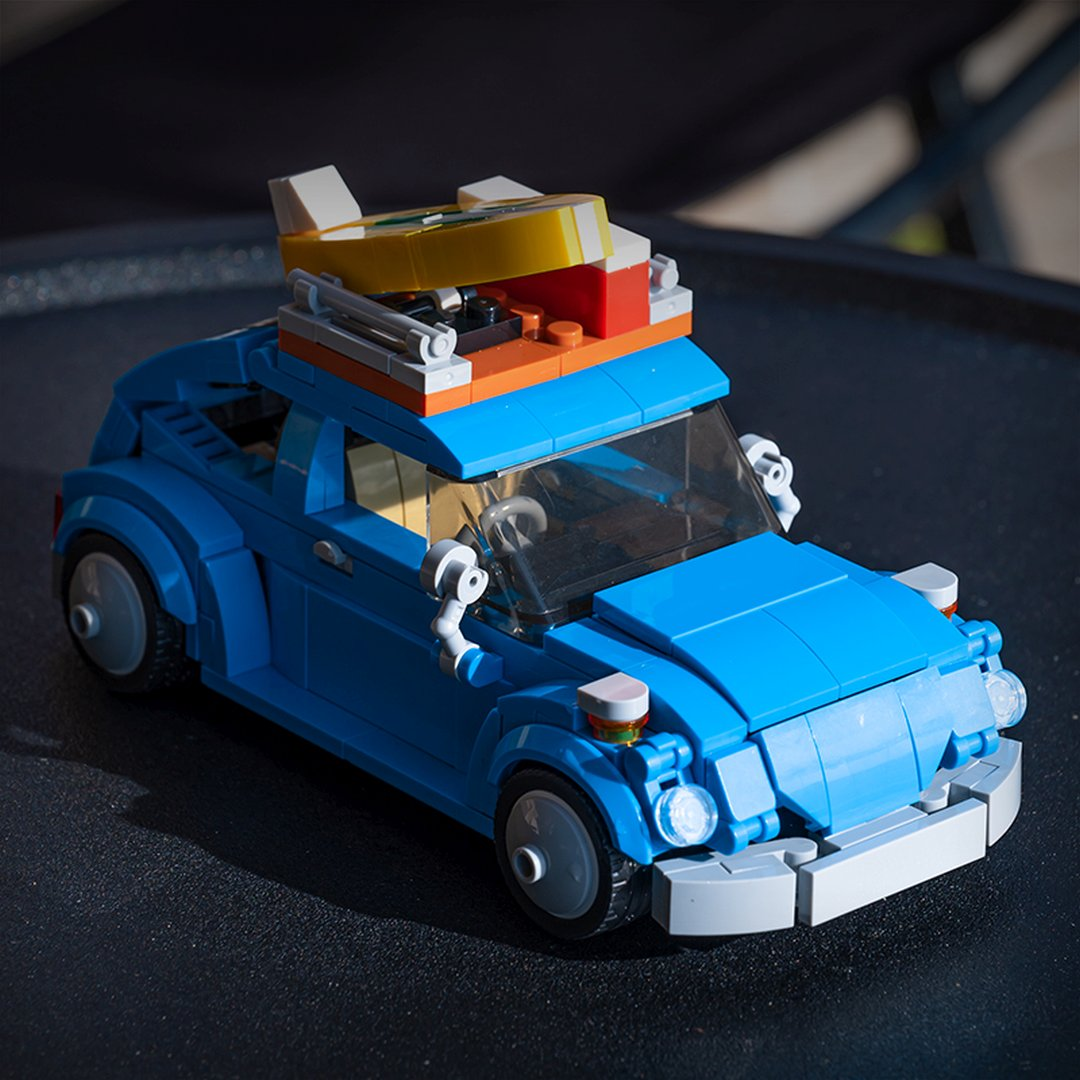 Niebieski samochód Lego z deską surfingową i bagażami na dachu.