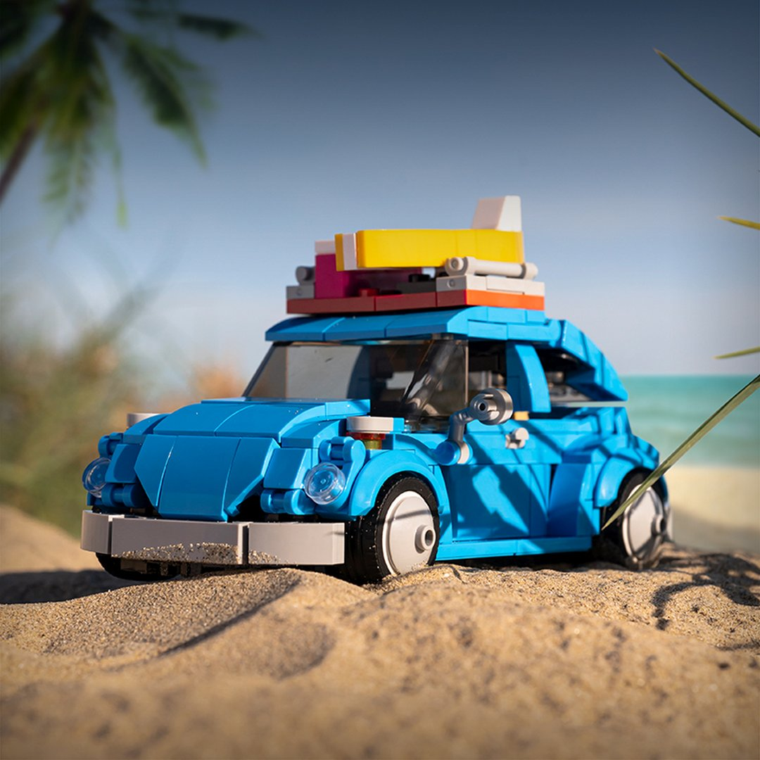Niebieski samochód Lego Garbus z bagażem na dachu stoi na plaży.