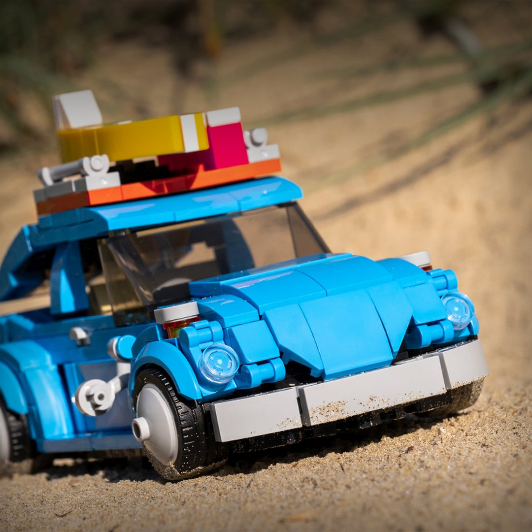 Niebieski samochód Lego z deską surfingową na dachu stoi na piasku.