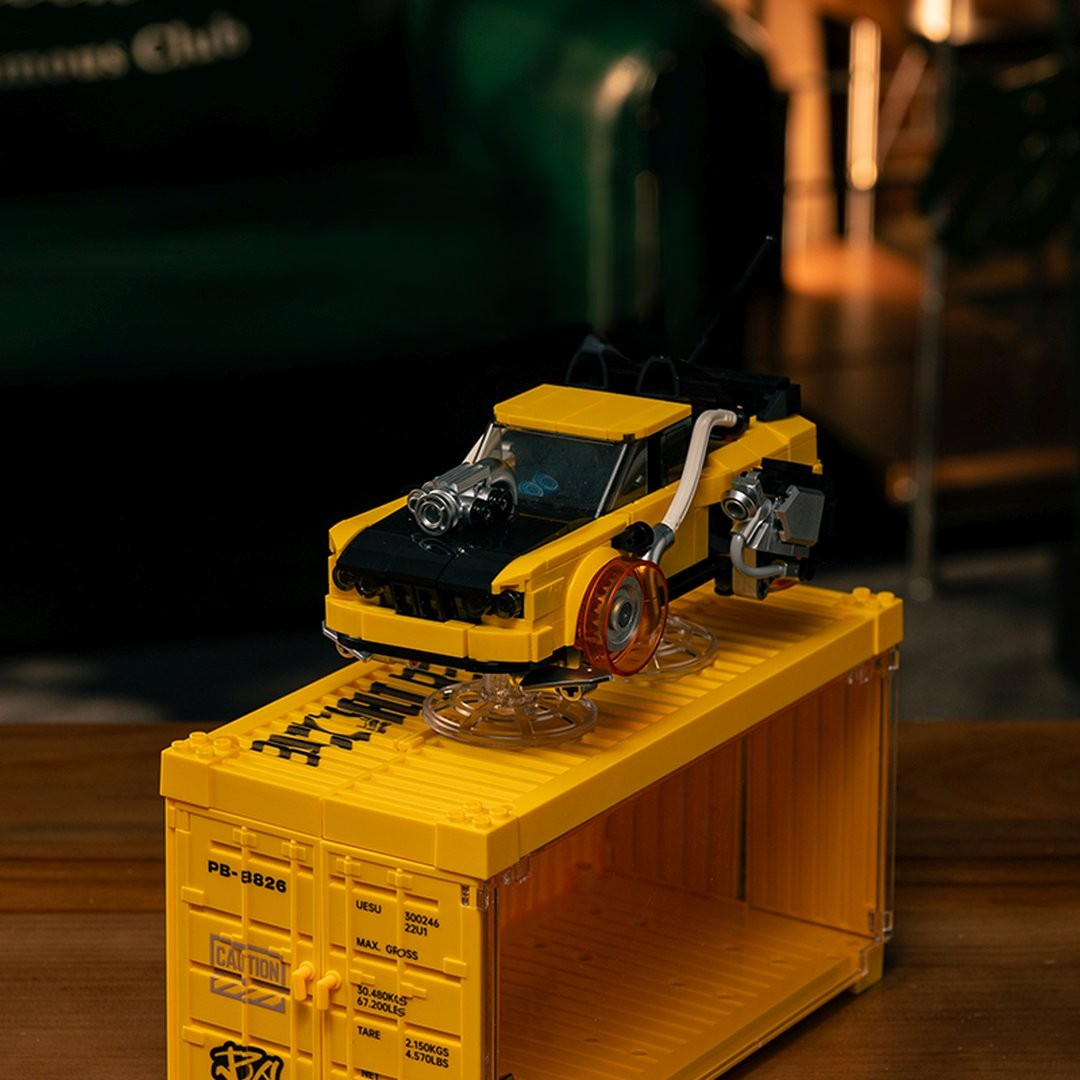 Żółty samochód Lego z srebrnym silnikiem siedzi na żółtym kontenerze Lego.