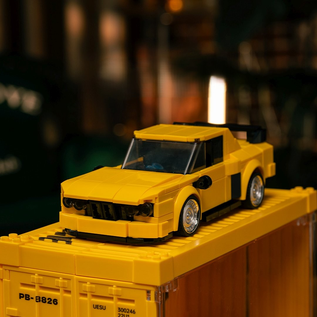 Żółty samochód z klocków Lego ze spojlerem stoi na żółtym kontenerze Lego.