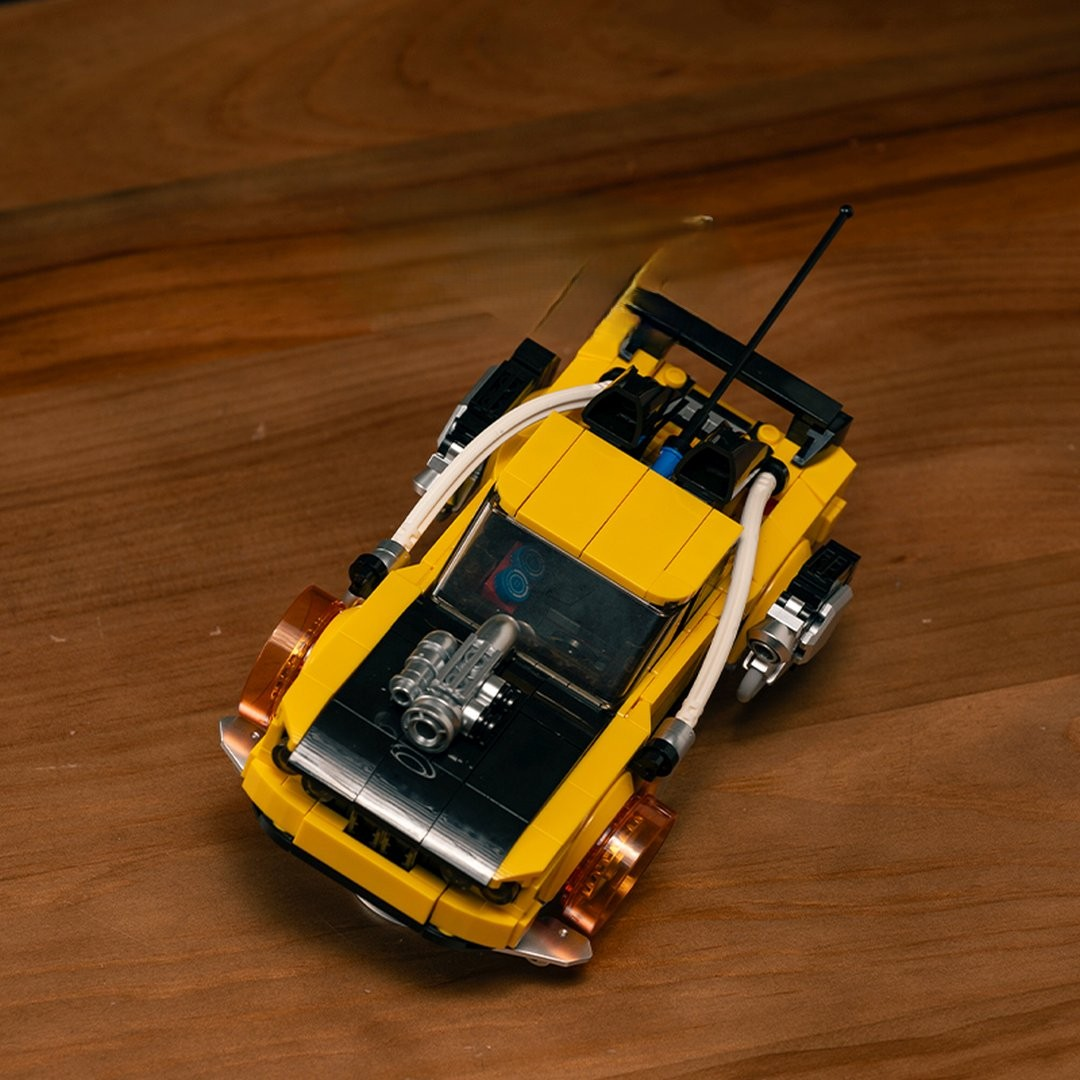 Żółty samochód Lego z czarnymi akcentami i silnikiem na masce, na drewnie.
