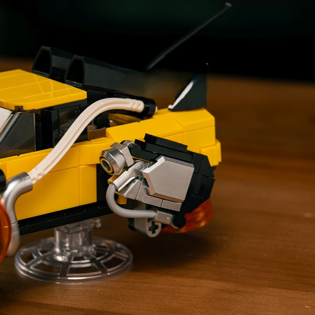 Żółty samochód Lego ze srebrnymi detalami silnika i przezroczystą podstawą.