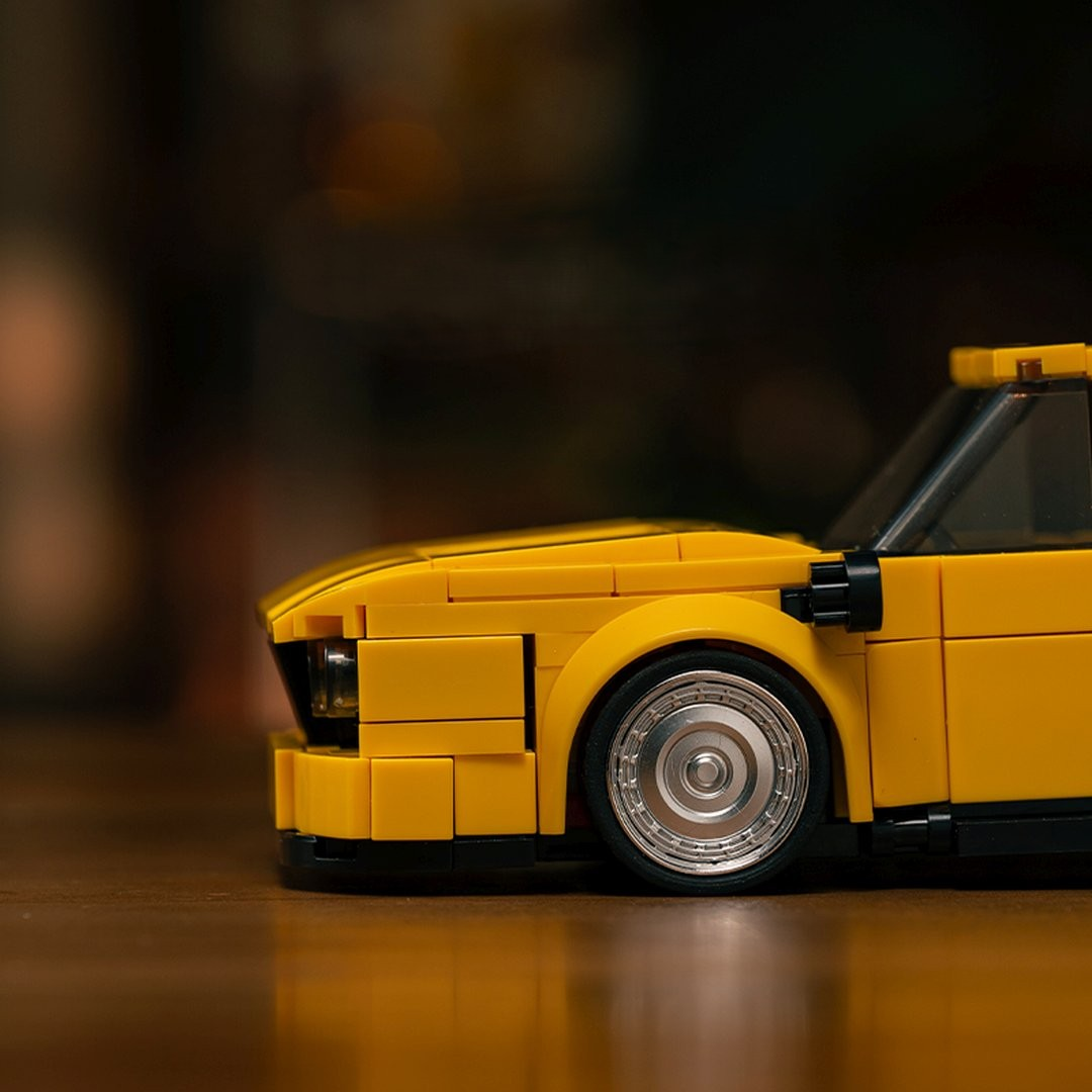 Żółty samochód Lego z srebrnymi felgami stoi na drewnianym stole.