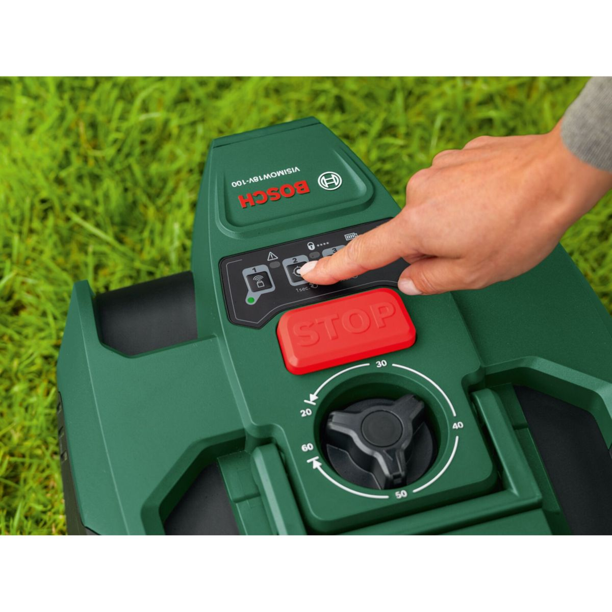 Eine Hand drückt die Stopp-Taste eines grünen Mähroboters auf gemähtem Gras.