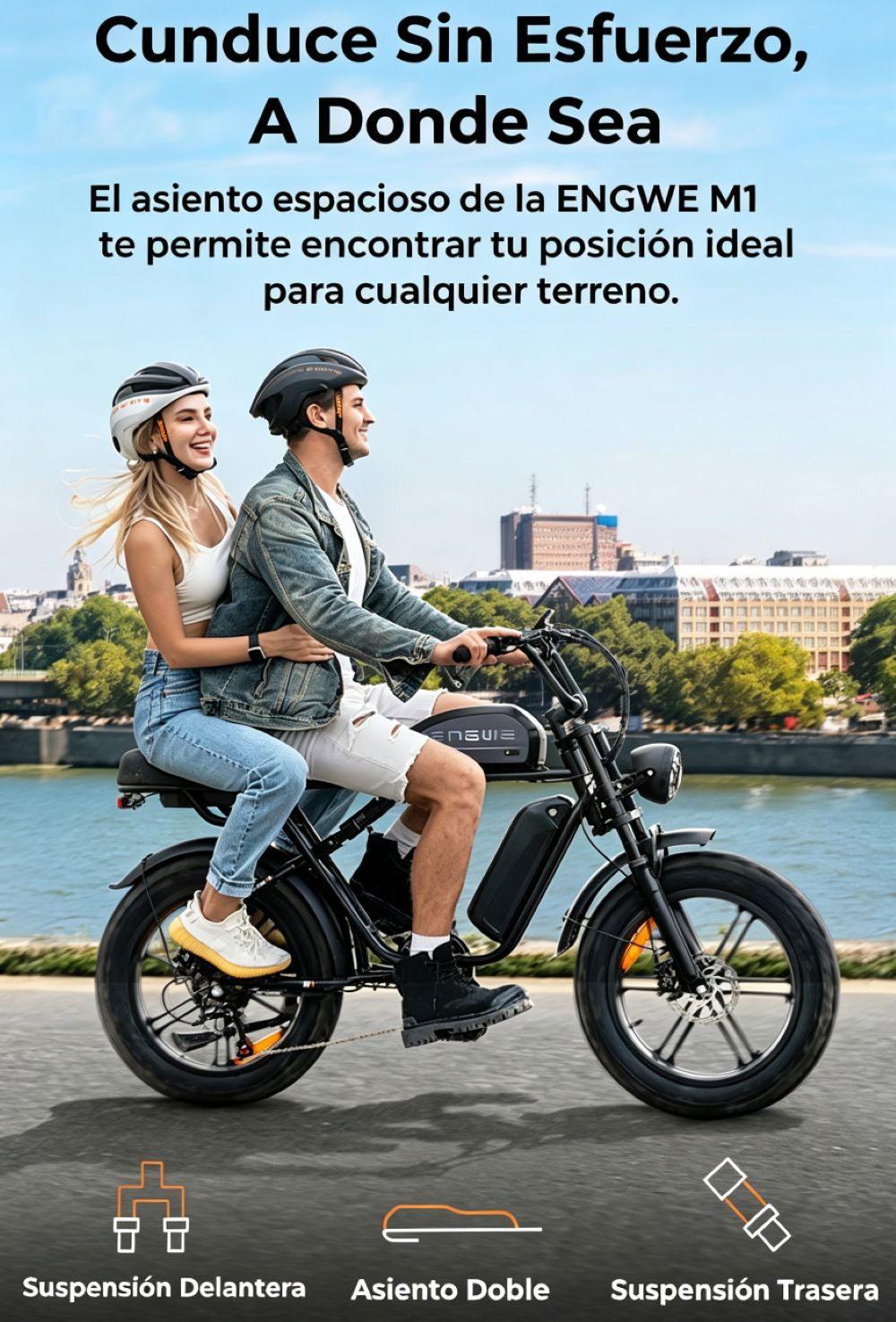 Una pareja monta en una e-bike negra junto a un río con edificios al fondo.