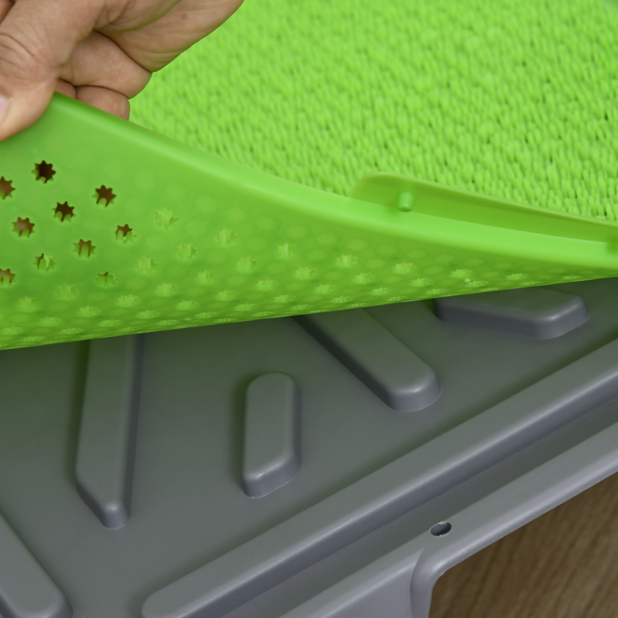 Mano solleva tappetino verde con fori a stella su base grigia.