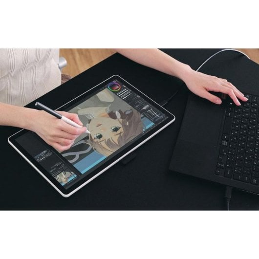 Una persona dibujando digitalmente una chica anime en una tableta junto a un portátil.