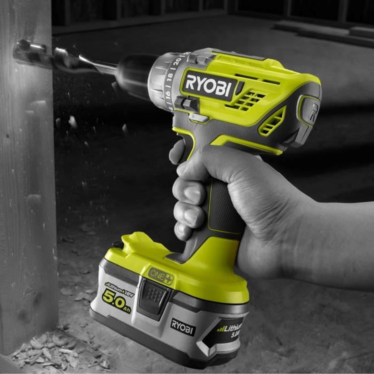 Una mano sostiene un taladro Ryobi amarillo, perforando un agujero en madera.