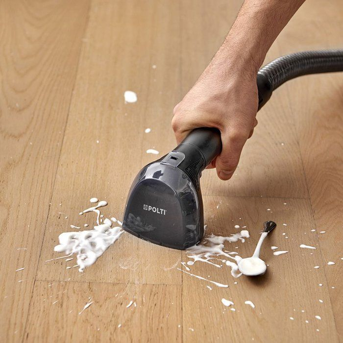 Ein Mann reinigt einen Holzboden mit einem Dampfreiniger, der weiße Flüssigkeit aufsaugt.