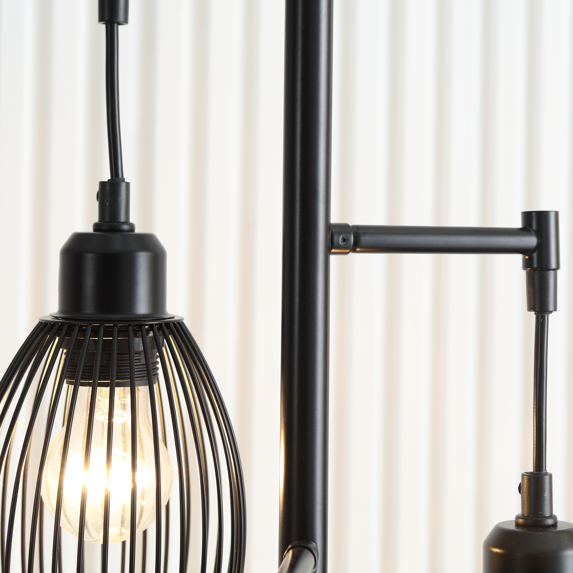 Primo piano di una lampada nera con paralume in filo e lampadina, su sfondo bianco.