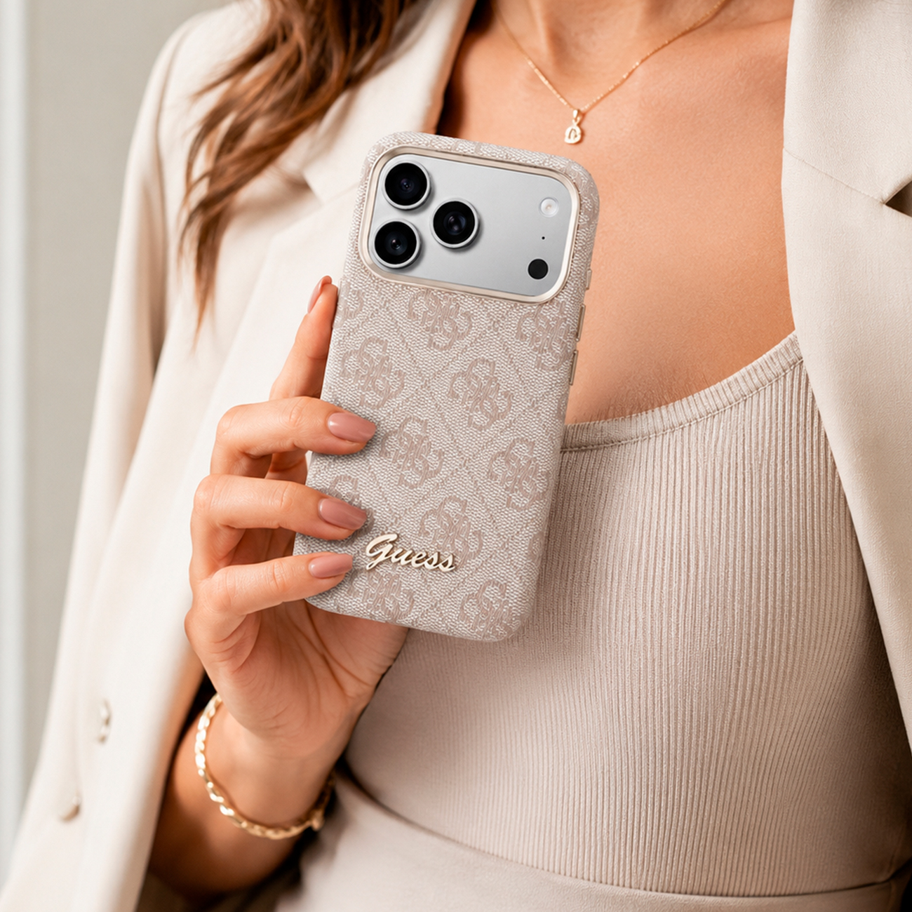 Una mujer sostiene un teléfono con logo Guess en un patrón beige.