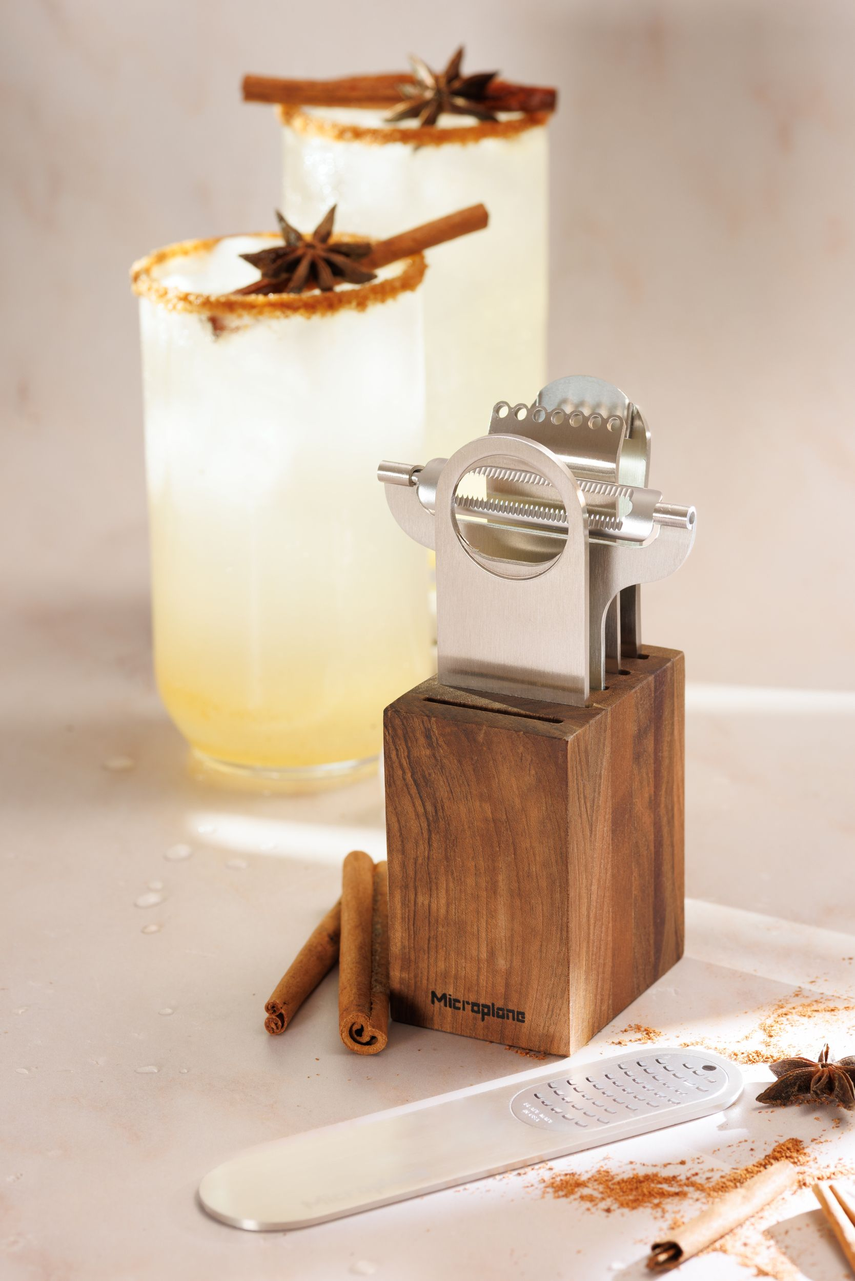 Zwei Cocktails mit Zimt, Sternanis. Ein Zester und ein Holzblock stehen daneben.