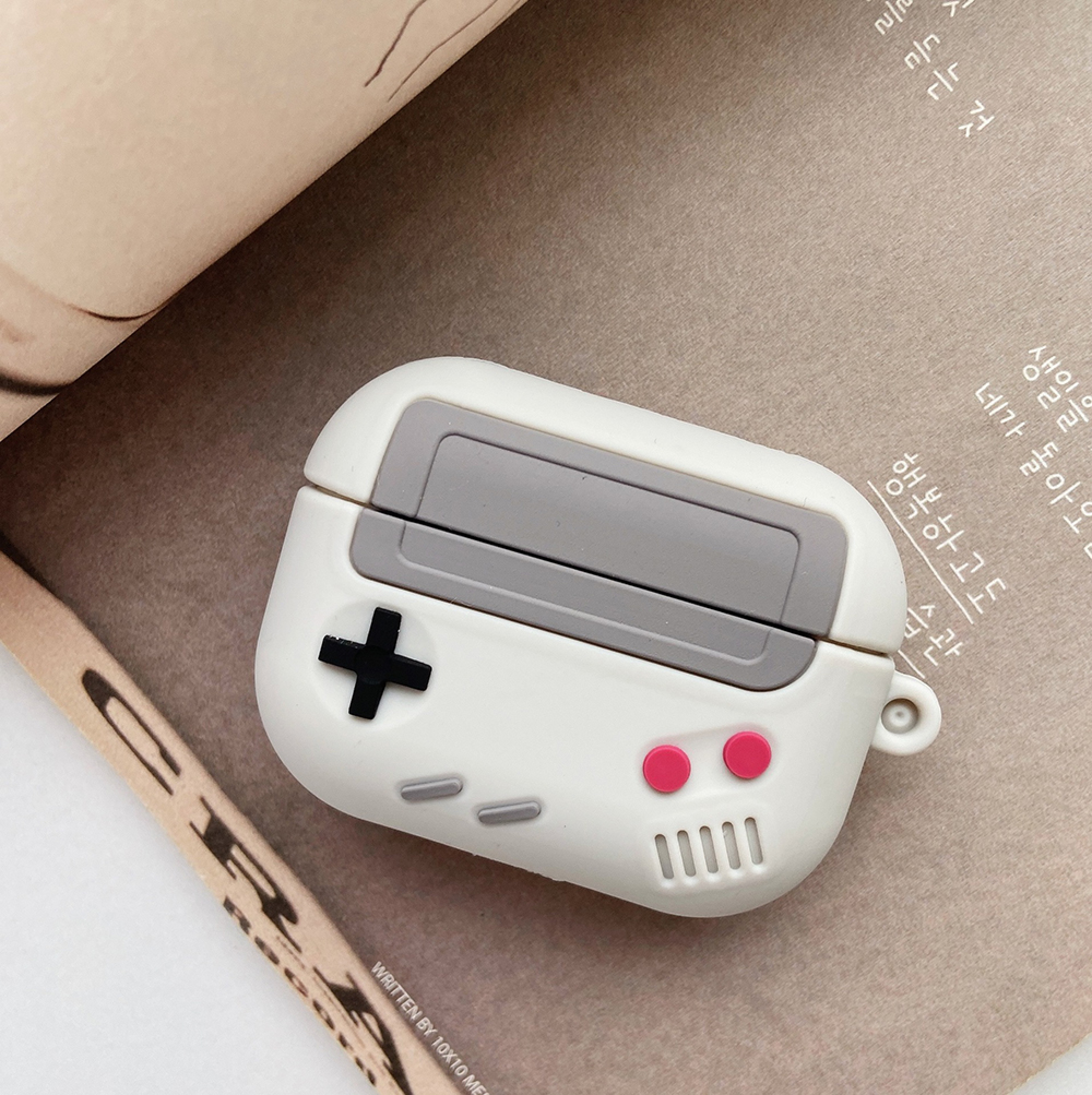 Ein weißes AirPod-Etui im Retro-Gaming-Design mit schwarzen und roten Knöpfen.
