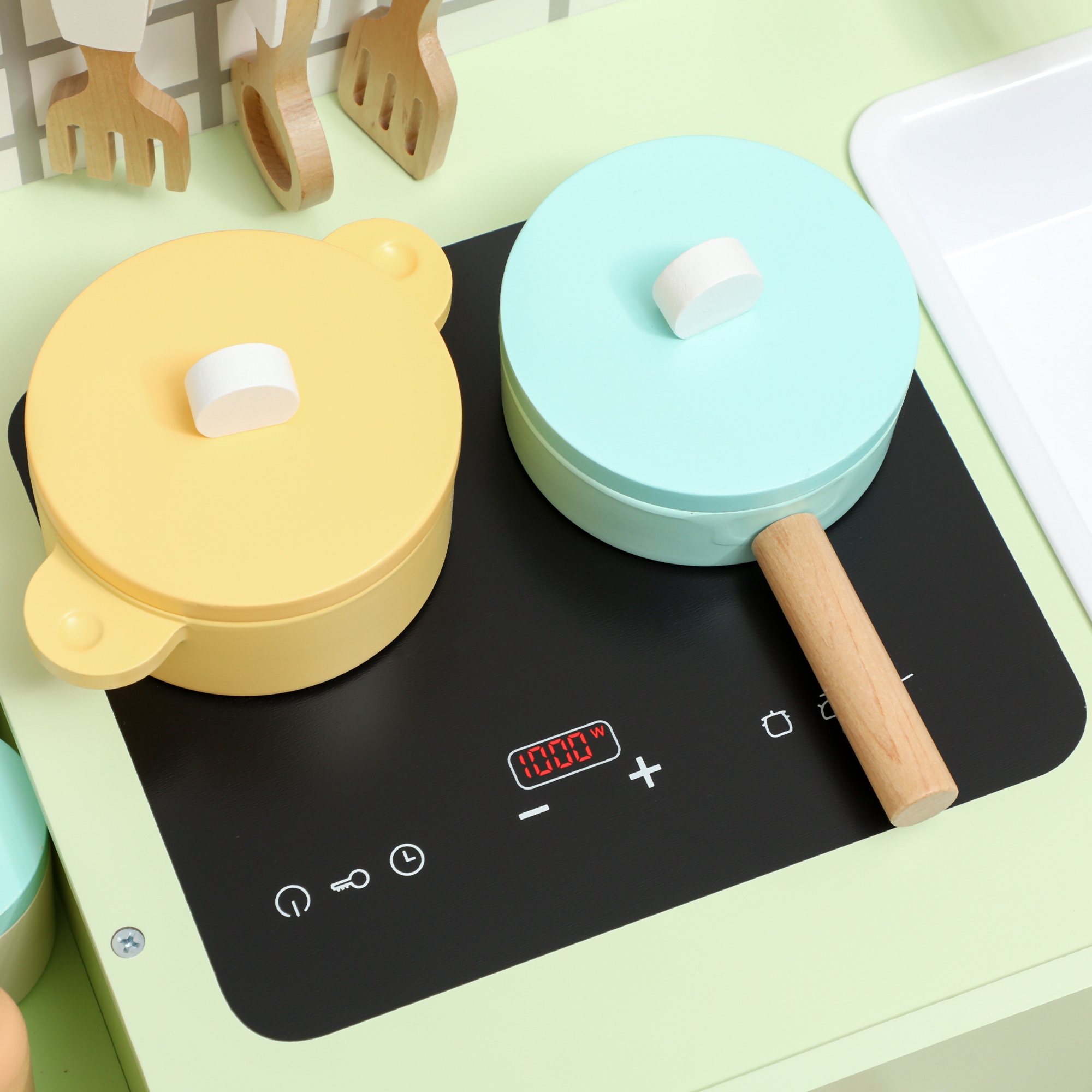 Cucina giocattolo con pentole gialle e turchesi su piano cottura nero. Utensili in legno appesi sopra.