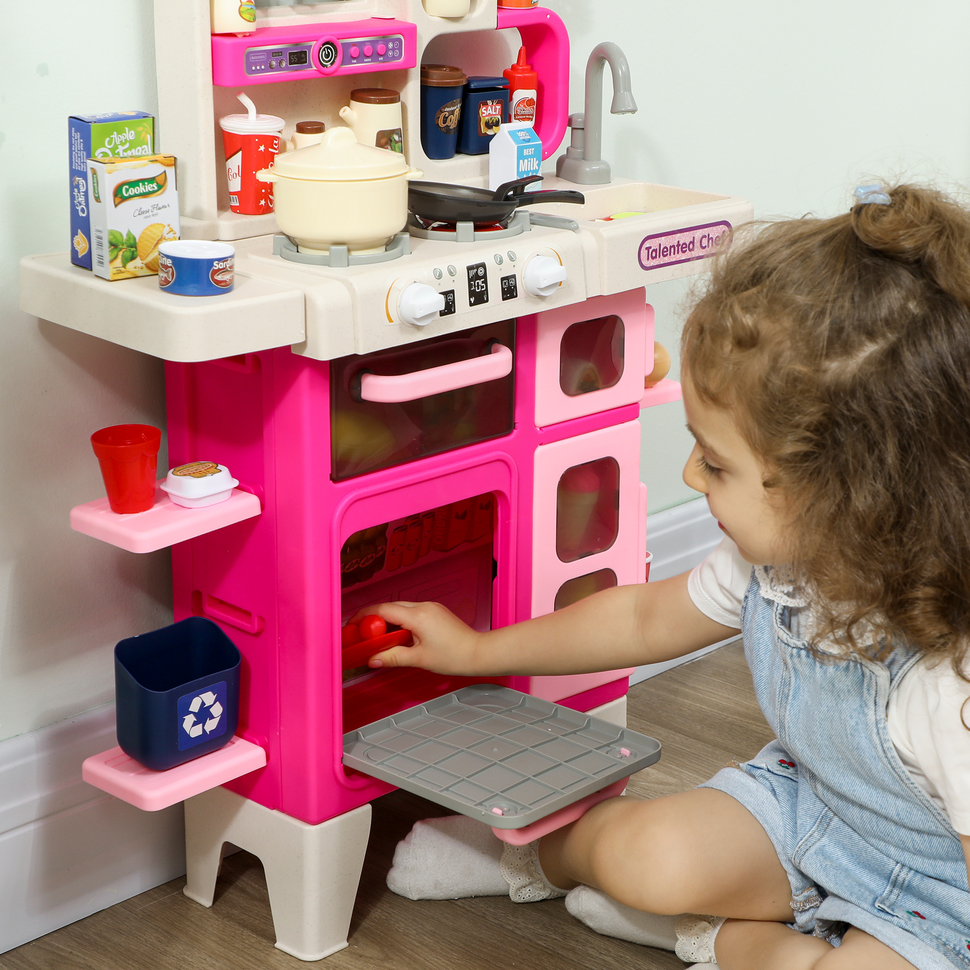 Una bambina gioca con una cucina giocattolo rosa con pentole, bottiglie e lavello.