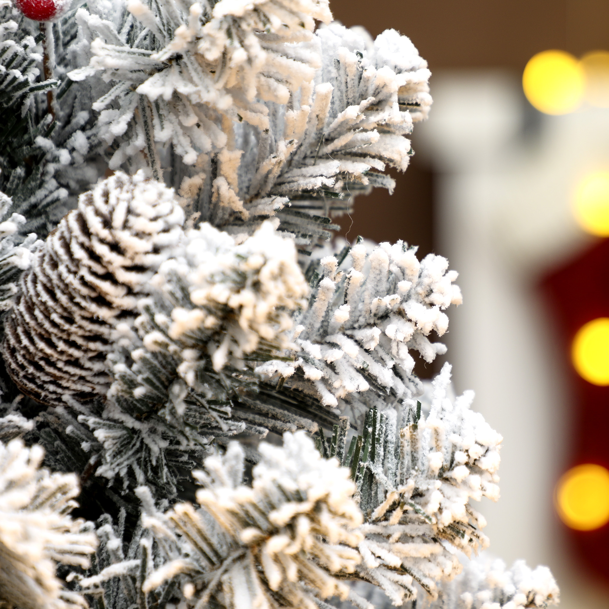 Una pigna e una bacca rossa su un ramo di albero di Natale innevato.
