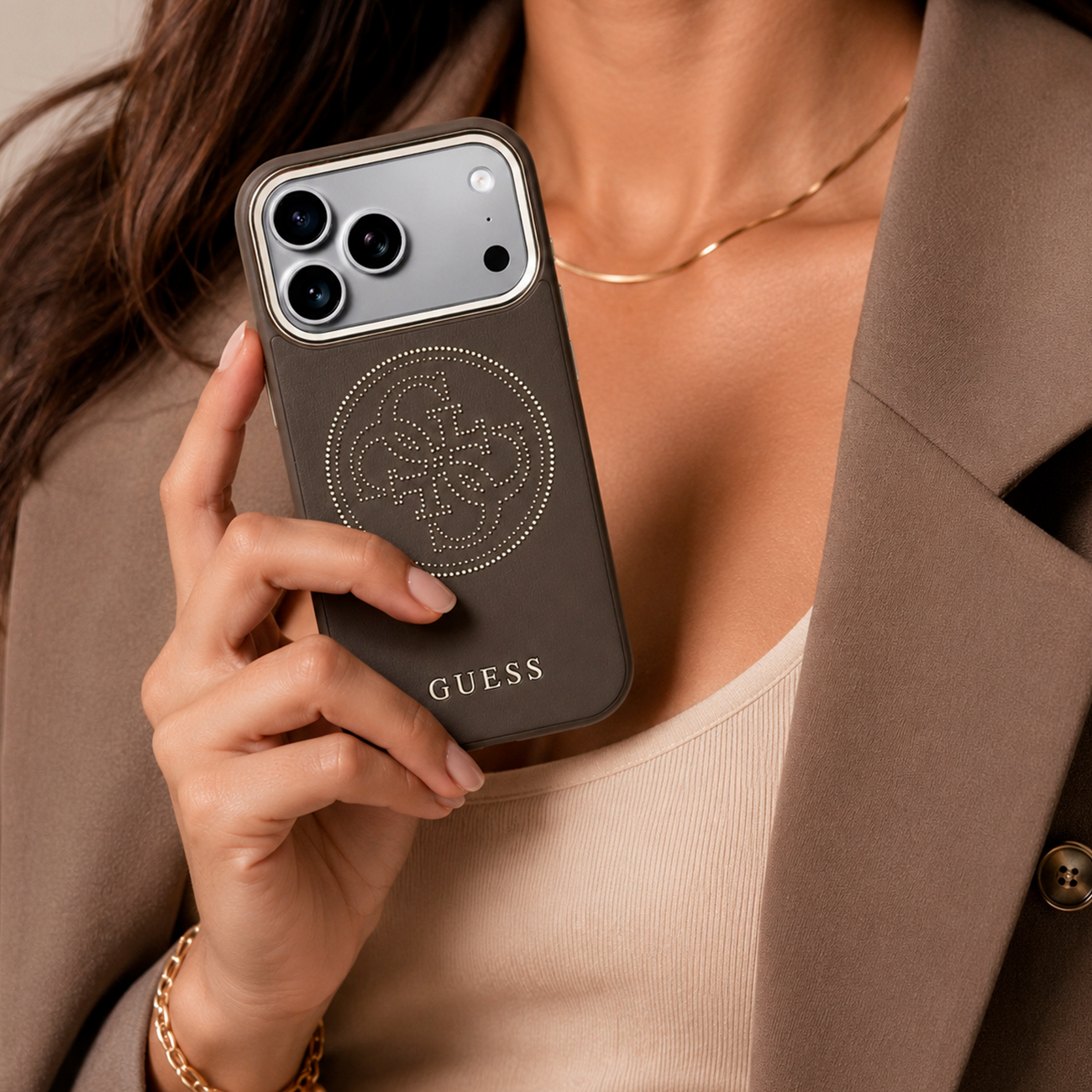 Una mano sostiene una funda marrón para smartphone con logo Guess y cámara.