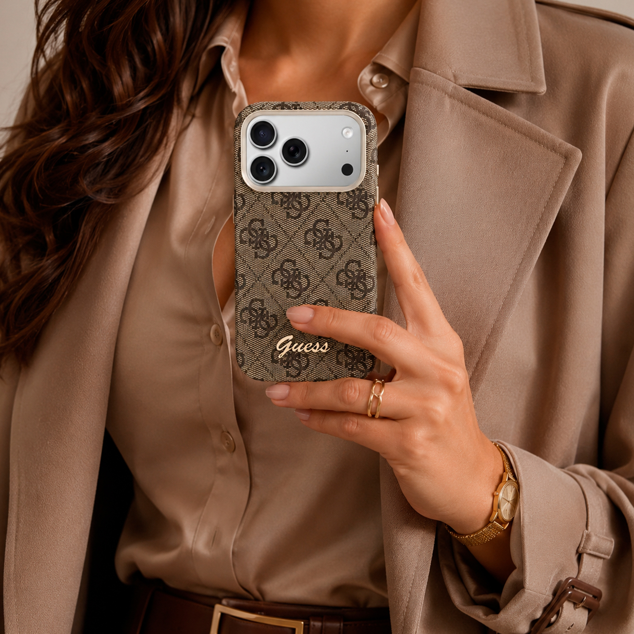 Mujer con abrigo beige sostiene funda marrón Guess con logo dorado.