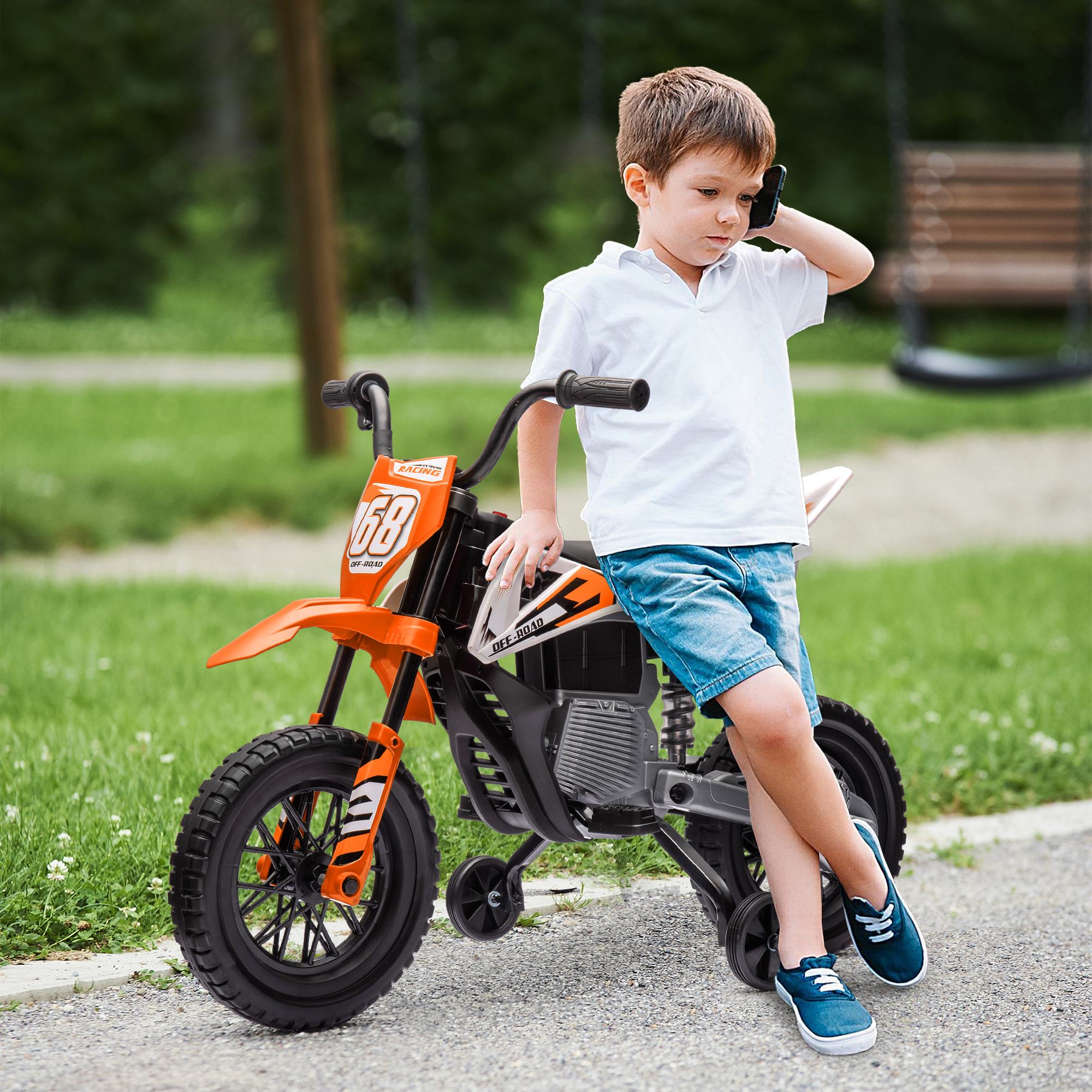 Un ragazzo in camicia bianca e pantaloncini di jeans parla al telefono accanto a una moto giocattolo arancione all'aperto.