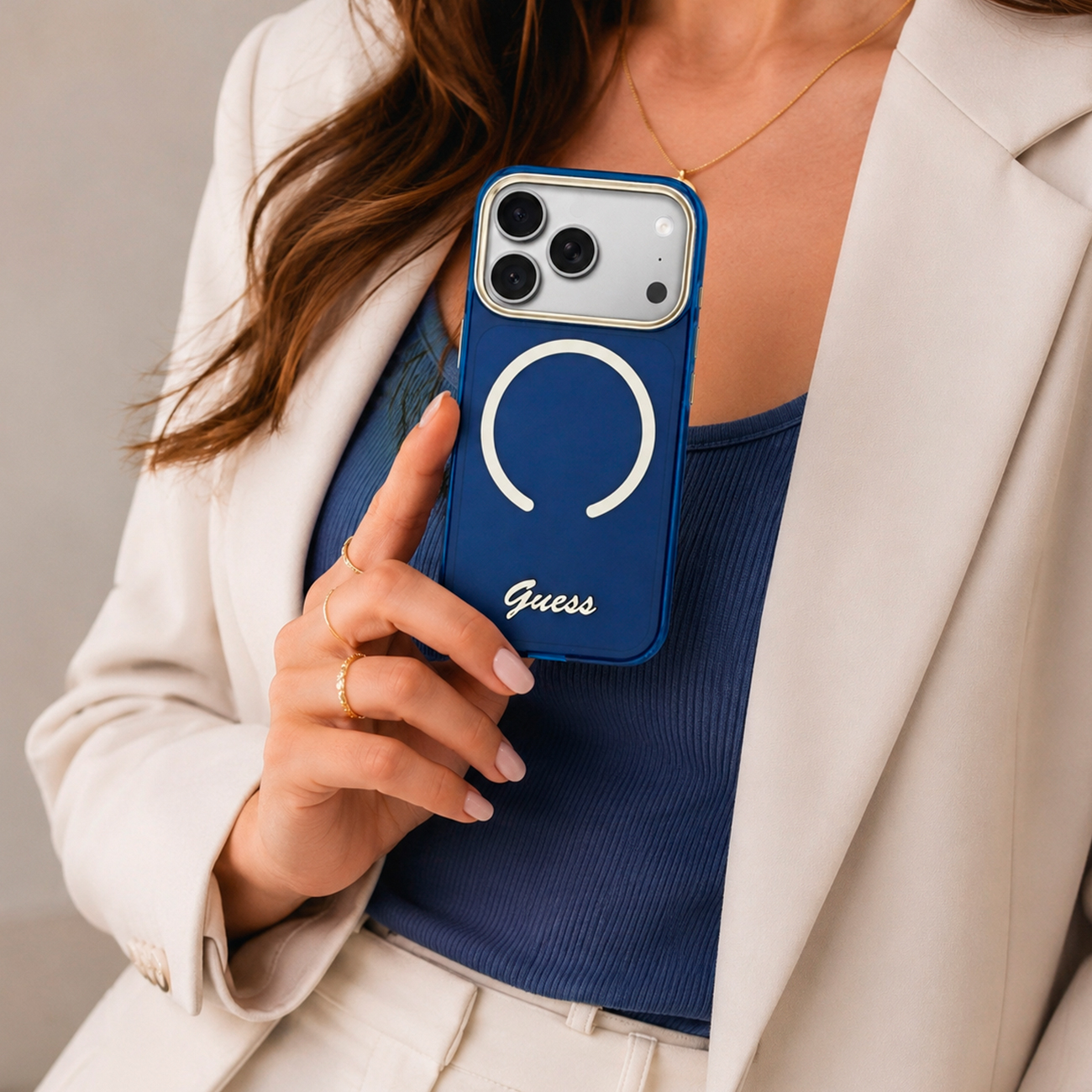 Una mujer sostiene una funda de teléfono azul con el logo de Guess y tres cámaras.