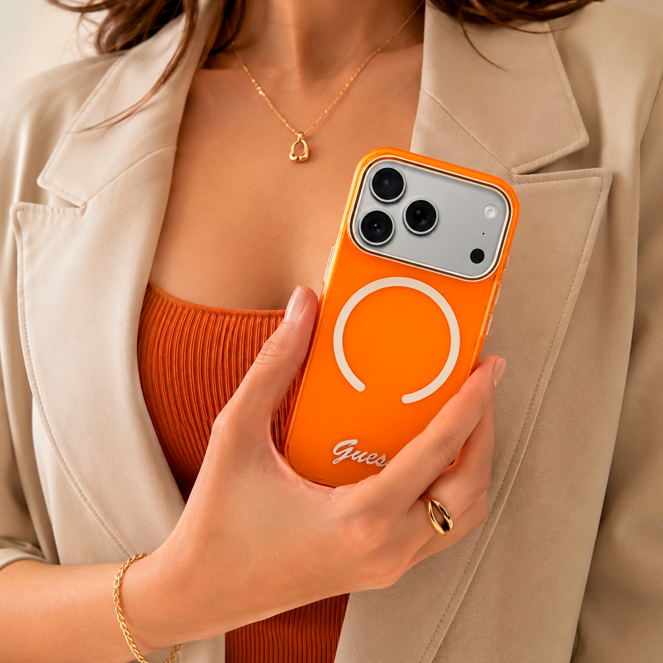 Una persona sostiene un teléfono naranja con círculo blanco y logo 'Guess'.