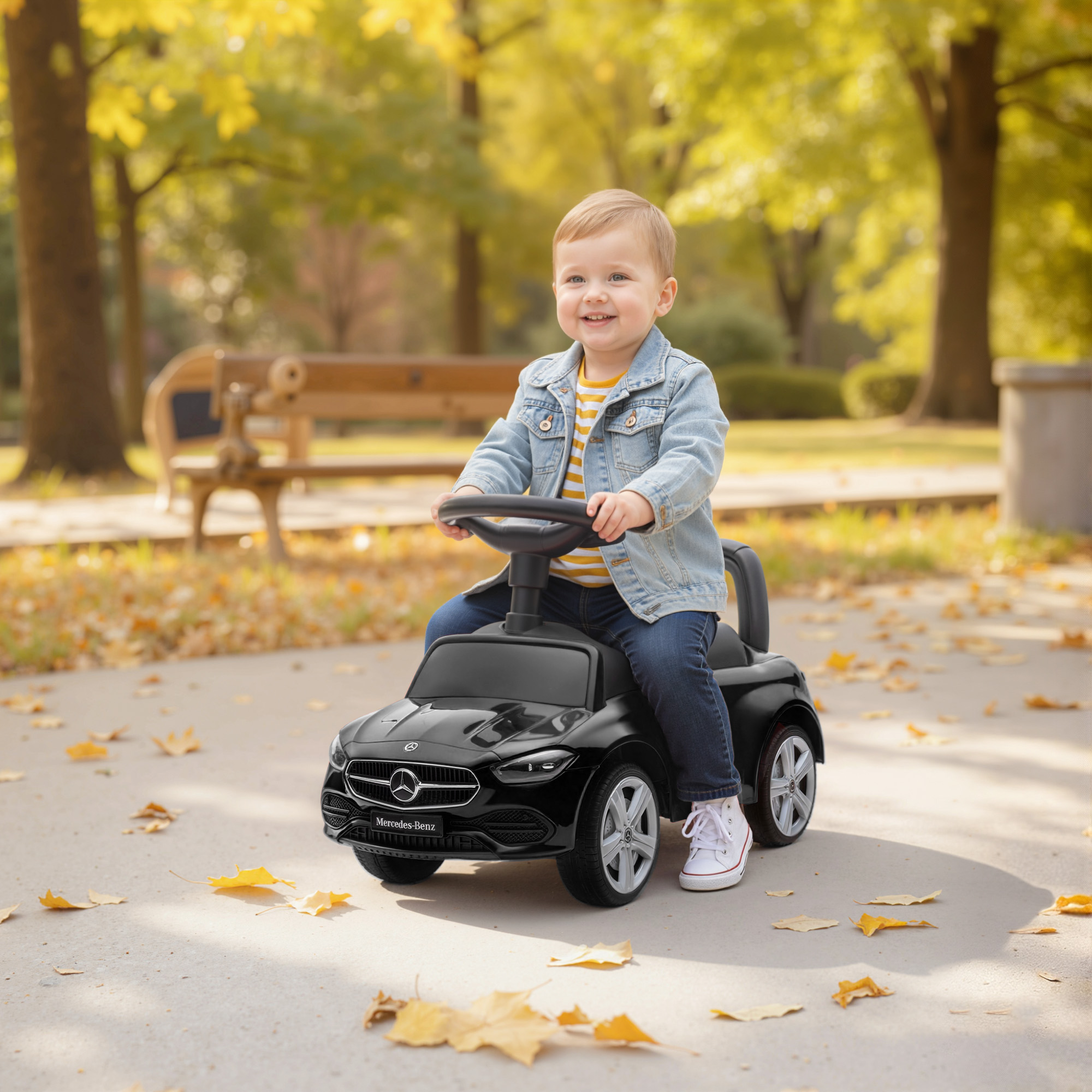 Un bimbo guida un'auto giocattolo nera su un sentiero nel parco autunnale.