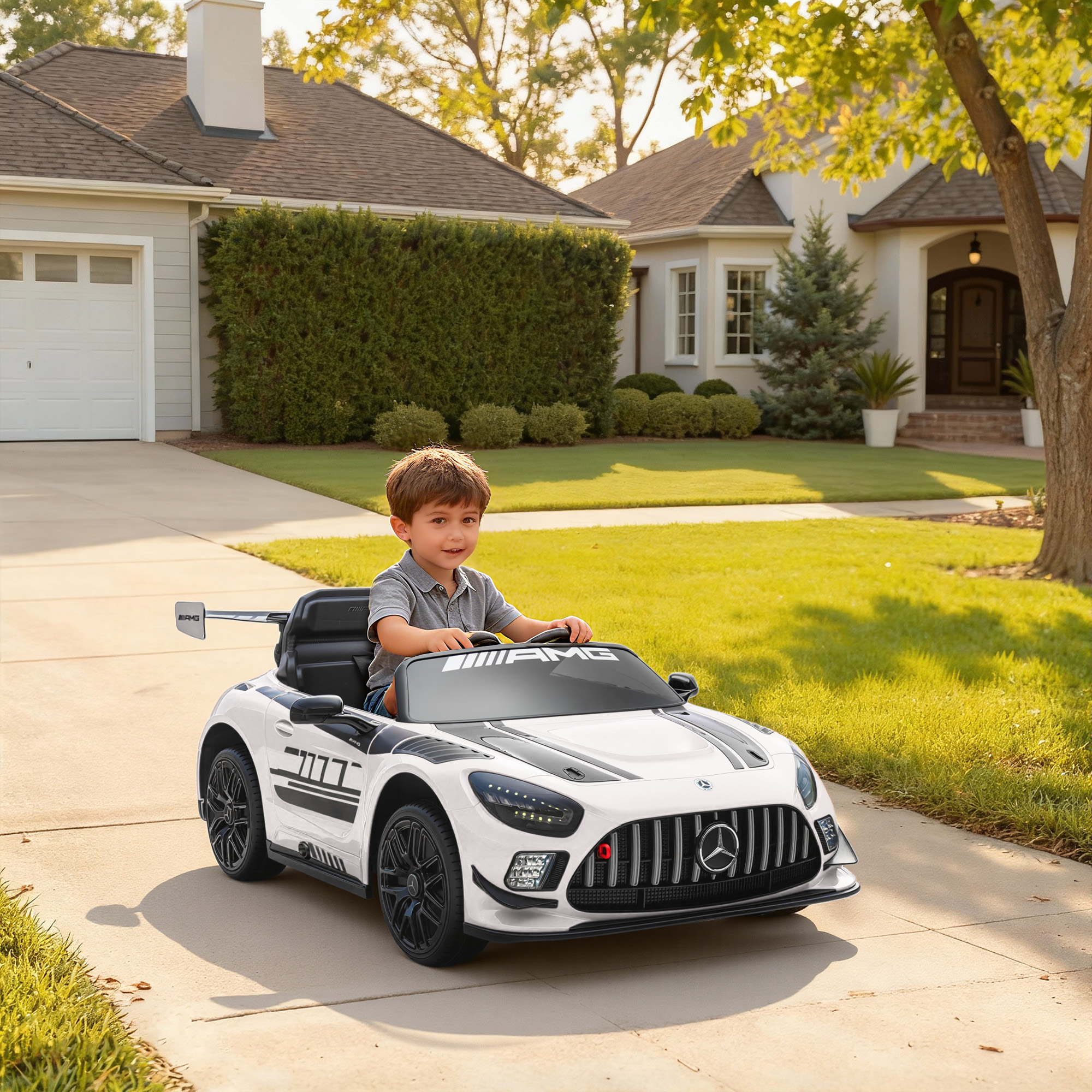 Un bambino guida un'auto giocattolo bianca con marchio AMG su un vialetto.