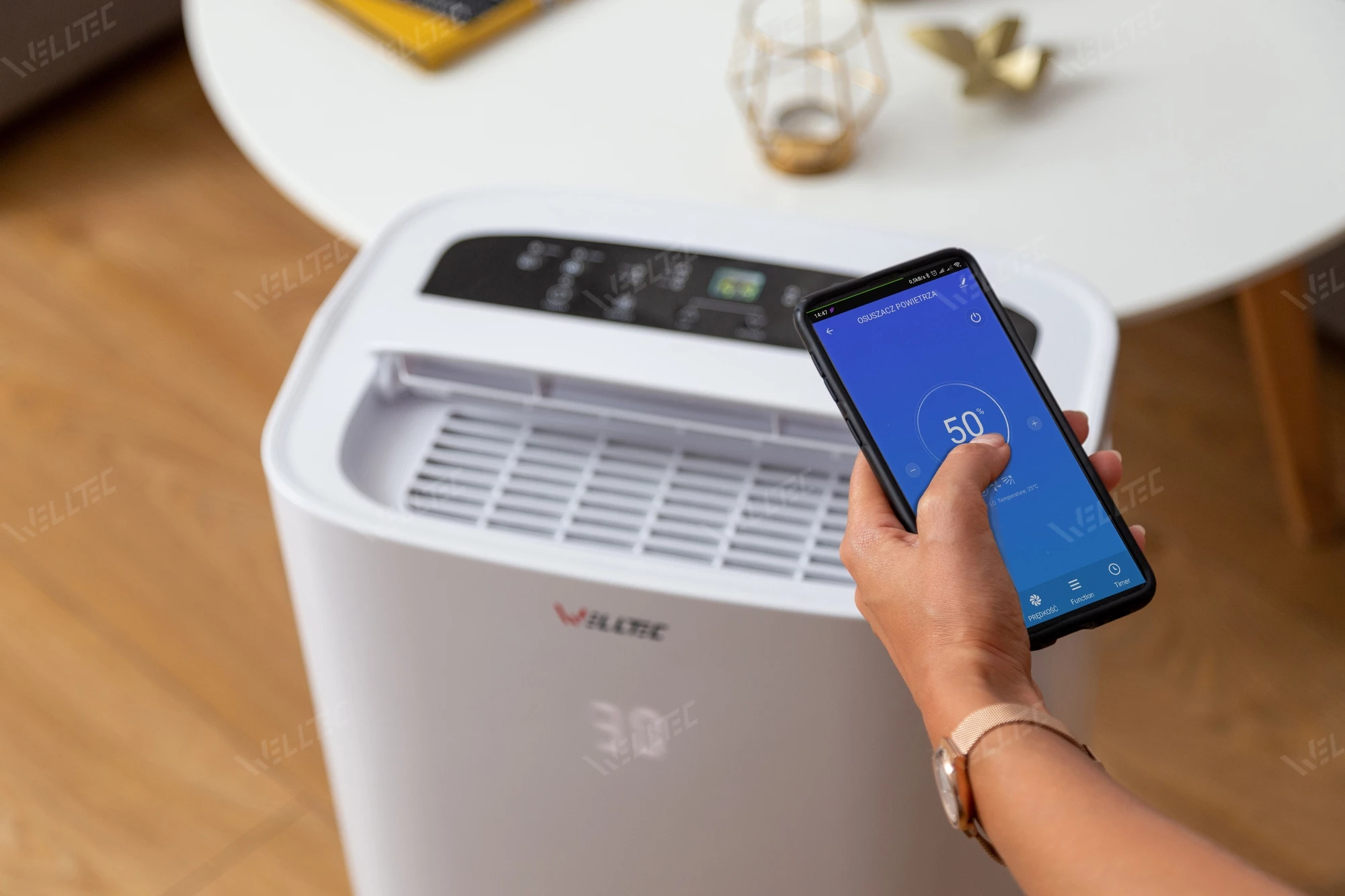Dłoń trzyma smartfon sterujący osuszaczem powietrza. Wyświetlono 50%.