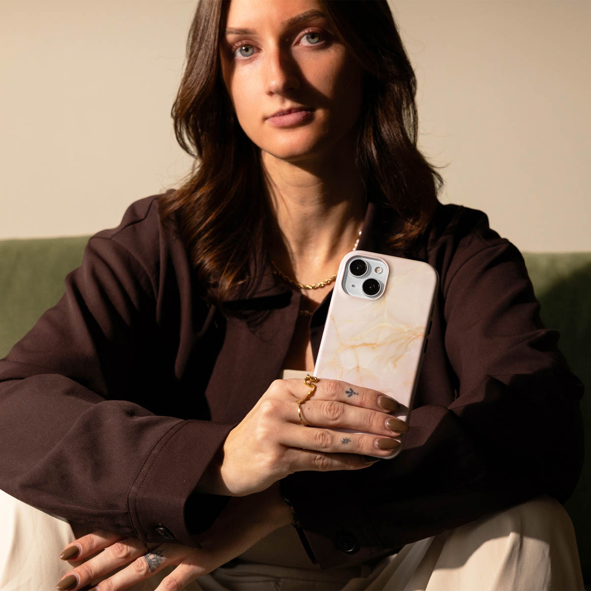 Una donna in blazer marrone tiene un telefono con motivo marmorizzato.
