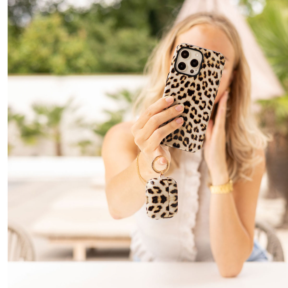 Una donna tiene un telefono con stampa leopardata e custodia AirPods abbinata.