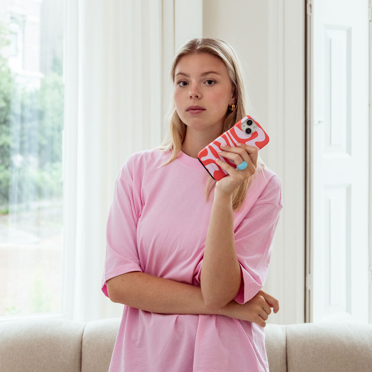 Una joven con camiseta rosa sostiene un teléfono con estampado rojo y blanco.