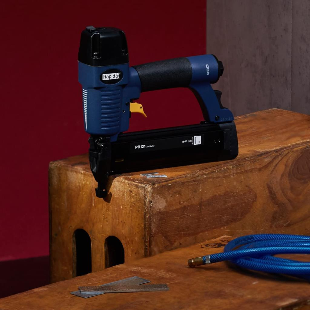 Una sparapunti pneumatica Rapid blu e nera su legno, con chiodi e tubo nelle vicinanze.