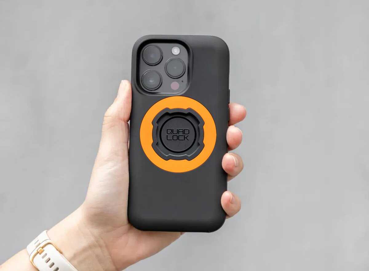 Eine Hand hält ein schwarzes iPhone mit orangefarbenem Quad Lock-Ring und drei Kameras.